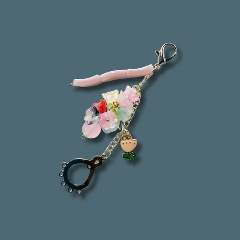 Decorative keychain with floral elements and a pink hair clip on a dark blue background
