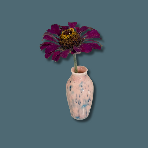 Pink speckled vase with a purple flower on a solid background