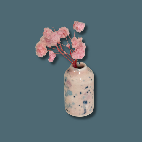Speckled ceramic vase with pink flowers on a solid background