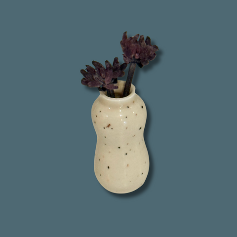 Small ceramic vase with purple flowers on a solid background