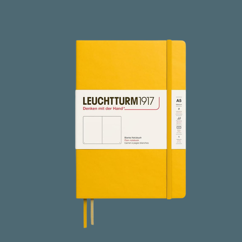 A Leuchtturm1917 A5 hardcover notebook in sunflower yellow with a white paper band around the middle, shown on a muted blue-gray background.