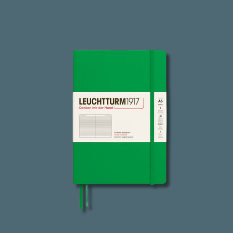 A Leuchtturm1917 A5 notebook with a vibrant green cover and a white paper label, shown on a solid slate gray background.