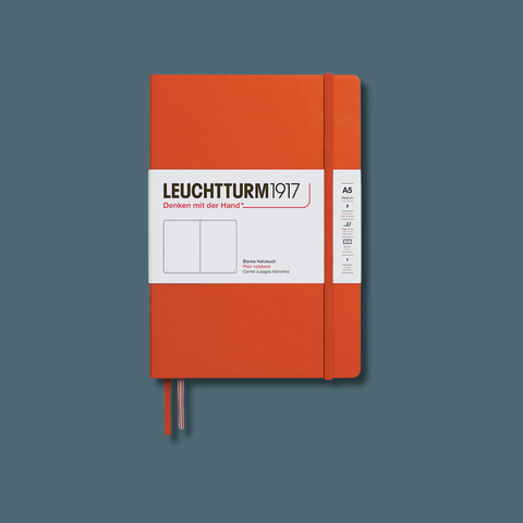 An orange hardcover notebook with a white paper band labeled 'LEUCHTTURM 1917' and a white size label, shown standing upright against a muted blue-gray background.