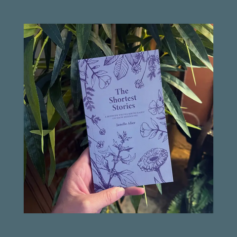 Hand holding a book titled 'The Shortest Stories' with floral designs against a plant background